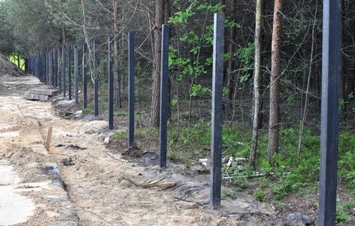 Rząd czarnych słupków kompozytowych EKOFORME wkopanych wzdłuż drogi pod ogrodzenie bazy materiałowej